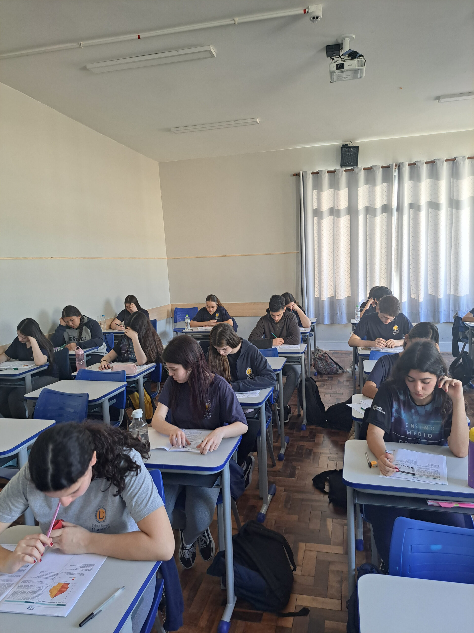 Imagem mostra alunos em sala de aula, realizando uma prova.